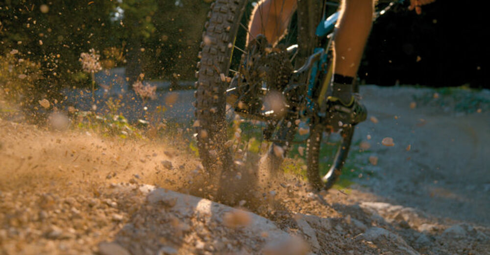 CLOSE UP, DOF: Mountain biker kicking up dust and rocks while br