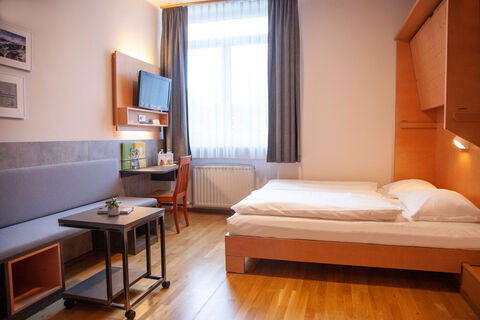 Familienzimmer FF4 mit TV, Fenster und Doppelbett im JUFA Hotel