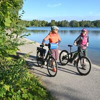 Radler schieben ihre Räder am Olchinger See