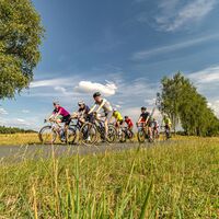Rennradgruppe untwerwegs durch Wiesen und Wolkenspiel