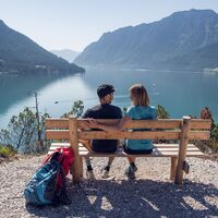 Bei herrlichem Wetter unterbricht ein Paar seine Wanderung am Gaisalmsteig, um auf einer Holzbank Rast zu machen und den Moment zu genießen.