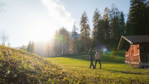 Herbstwanderung am Oberen Wiesenweg_Paar läuft auf Wiese vor Holzhütte_Aufnahme gegen die Sonne.jpg