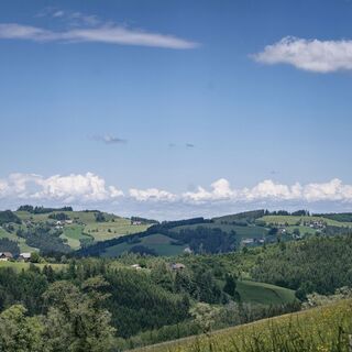 Das Bild zeigt die grünen Hügel des Steyrtals und einen blauen Himmel mit vereinzelten Wolken.