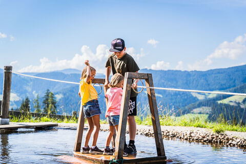 Der Flori's Erlebnispfad ist das Wander-Highlight für Kids in Flachau. Am Bild zu sehen sind 3 Kids auf am Floß.