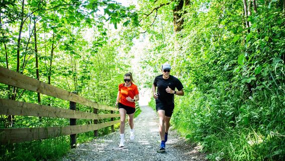 Der Urlaubsort Flachau  ist als Teil der Salzburger Sportwelt nicht nur zum Entspannen, sondern auch zum Sporteln ideal. Das wunderschöne Bergpanorama lädt geradezu zum Laufen ein. Bei den verschiedenen Laufstrecken, ist für jeden was dabei. Im Bild sieht man zwei Sportler, die den Ortsrundweg entlang laufen. Sie laufen durch den Wald, an einem Zaun entlang.