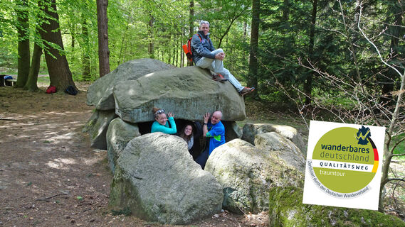 Wanderer beim Großsteingrab Steinfelder Holz mit Qualitätsweg-Logo