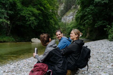drei Wander:innen sitzen am Fluss im Höllental