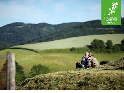Ein Wanderpärchen genießt die Aussicht auf sanfte Hügel und bewaldete Höhen.