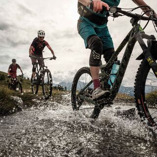 Mountainbiker überqueren einen Bach am Gibidum-Pass