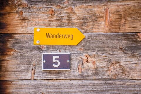 Wanderweg-Schild sowie Hausnummern-Schild (Nr. 5) an holziger Hauswand in Brienzwiler