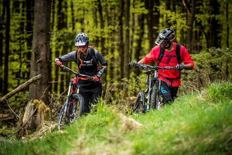 2 Mountainbiker schieben ihre Bikes über eine Lichtung
