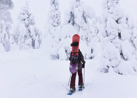 Snowboarder wandert mit Schneeschuhen zum Valtavaara-Gipfel