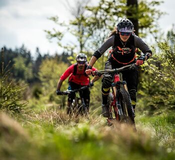 2 Mountainbiker schieben ihre Bikes über eine Lichtung