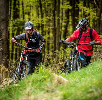2 Mountainbiker fahren über Gras an Büschen vorbei